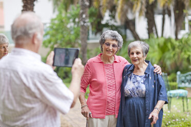 Senior man photographing friends in retirement villa garden - CUF36610