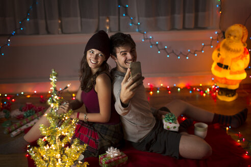 Young couple taking selfie in sitting room at christmas - ISF14445