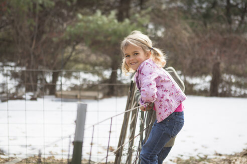 Young girl climbing wire fence in field - ISF14478