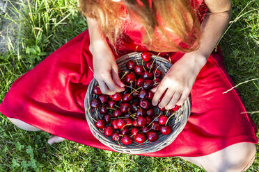 Mädchen mit Korb voller Kirschen auf einer Wiese sitzend, Teilansicht - SARF03813