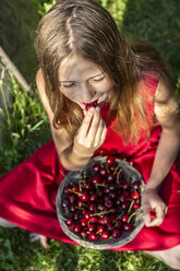 Girl sitting on a meadow eating cherries - SARF03814