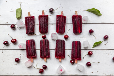 Homemade cherry ice lollies, ice cubes and cherries on white wood - SARF03823