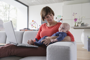 Mother and baby boy reclining on sofa with laptop - CUF36692