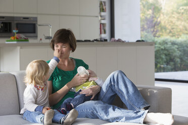 Mother, baby boy and female toddler sitting on sofa - CUF36697