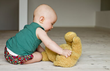Baby Mädchen spielt mit Teddybär auf dem Boden - CUF36760