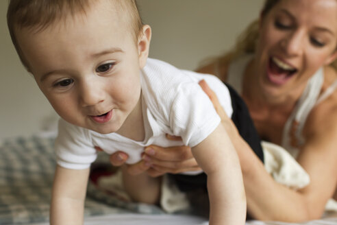 Mother guiding baby boy crawling on bed - CUF36880