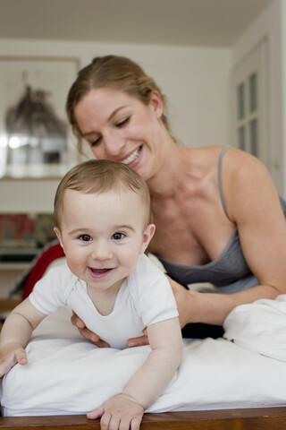 Mother guiding baby boy crawling on bed stock photo