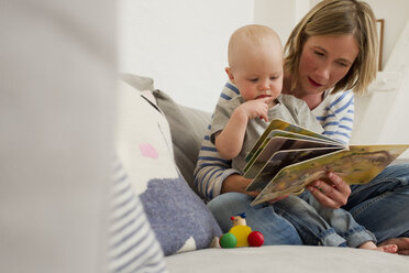 Ältere Mutter und kleine Tochter auf dem Sofa im Wohnzimmer lesen ein Bilderbuch - CUF36892