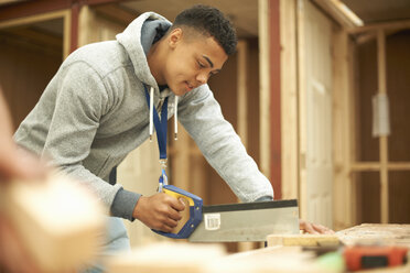 Male college student using saw in woodworking workshop - CUF36897