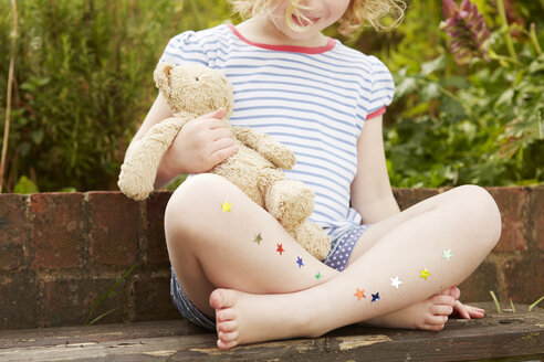 Mädchen auf Gartenstuhl mit Sternaufklebern an den Beinen - CUF36907