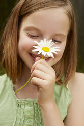 Portrait of girl in garden holding up daisy - CUF36916
