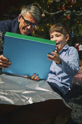 Father on sitting room floor opening christmas gifts with son - CUF36931