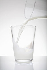 Fresh milk pouring from jug into drinking glass - CUF36963