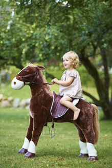 Porträt eines weiblichen Kleinkindes auf einem Spielzeugpferd im Garten - CUF36973