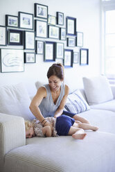 Mid adult mother tickling toddler daughter on sofa - CUF36976