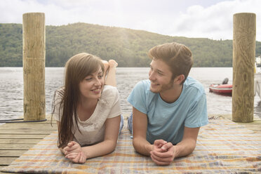 Young smiling couple lying on blanket on lakeside jetty - CUF36996