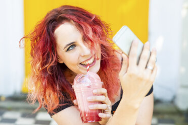 Porträt einer lachenden Frau, die ein Selfie mit ihrem Smartphone macht, während sie einen Smoothie trinkt - WPEF00481