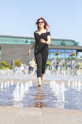 Junge Frau, die Spaß daran hat, durch einen Springbrunnen zu laufen - WPEF00487