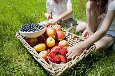 Cropped view of brother and sisters eating fruit from basket on grass - CUF37059