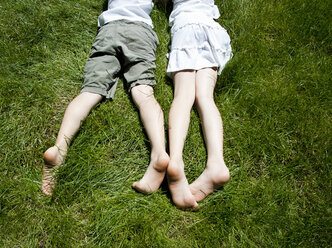 Draufsicht auf die Beine von Bruder und Schwester, wie sie im Gras liegen - CUF37060