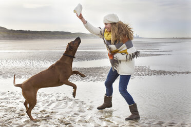 Mid adult woman teasing dog at beach, Bloemendaal aan Zee, Niederlande - CUF37123