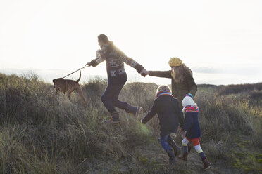 Ein erwachsenes Paar, das mit seinem Sohn, seiner Tochter und seinem Hund in den Sanddünen spazieren geht - CUF37126