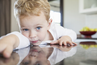 Portrait of three year old boy leaning forward on kitchen bench - CUF37131