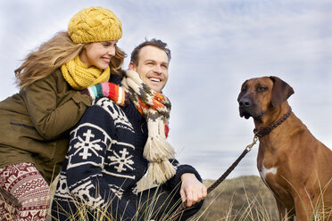 Smiling mid adult couple and dog at coast - CUF37138