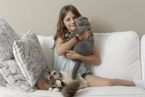 Mädchen mit zwei Katzen auf dem Sofa im Wohnzimmer - CUF37141