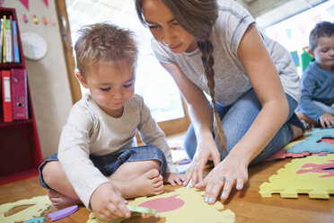 Lehrerin und Junge bei der Arbeit mit einem Puzzle im Kindergarten - CUF37147