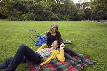 Young couple holding hands on picnic blanket in park - CUF37325