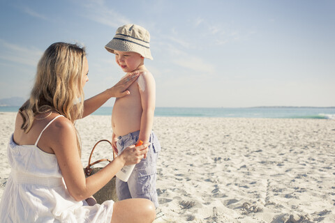 Mittlere erwachsene Mutter, die ihrem kleinen Sohn am Strand Sonnencreme aufträgt, Kapstadt, Westkap, Südafrika, lizenzfreies Stockfoto