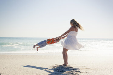 Mittlere erwachsene Mutter, die ihren kleinen Sohn an den Händen am Strand schwingt, Kapstadt, Westkap, Südafrika - CUF37342