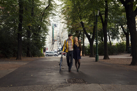 Junges Paar spaziert in einem von Bäumen gesäumten Park, lizenzfreies Stockfoto