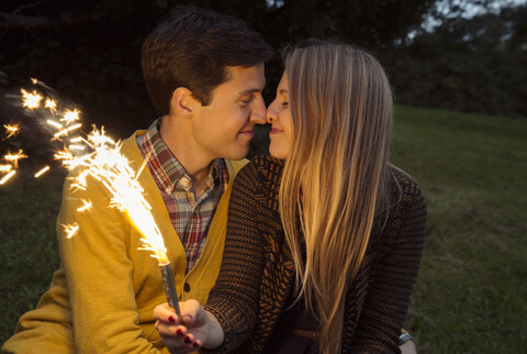 Junges Paar Nase an Nase im Park mit funkelndem Feuerwerk, lizenzfreies Stockfoto