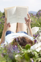 Junge Frau liegt im Feld und liest ein Buch - CUF37389