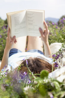 Young woman lying in field reading book - CUF37389