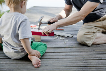 Male toddler watching father make toy boat on pier - CUF37436