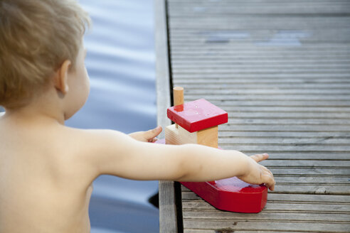 Rückansicht eines männlichen Kleinkindes, das mit einem Spielzeugboot am Pier spielt - CUF37438