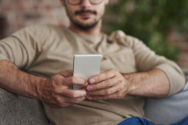 Mann auf Couch sitzend, Textnachrichten, Teilansicht - ABIF00654