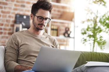 Porträt eines Mannes, der zu Hause auf der Couch sitzt und einen Laptop benutzt - ABIF00656