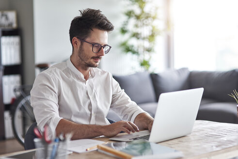 Businessman working on laptop at home office - ABIF00659