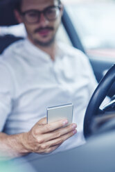 Hand of businessman sitting in car holding cell phone - ABIF00668
