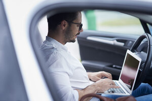 Businessman sitting in car working on laptop - ABIF00669