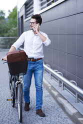 Geschäftsmann am Telefon, der sein Fahrrad schiebt - ABIF00670