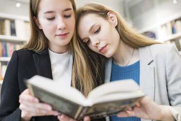 Porträt von zwei Mädchen im Teenageralter, die in einer öffentlichen Bibliothek gemeinsam ein Buch lesen - WPEF00491