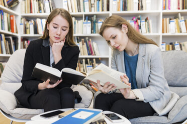 Zwei Mädchen im Teenageralter sitzen in einer öffentlichen Bibliothek und lesen Bücher - WPEF00492