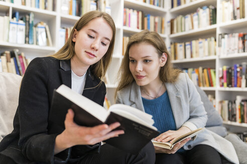 Porträt von zwei Mädchen im Teenageralter, die in einer öffentlichen Bibliothek sitzen und sich ein Buch ansehen - WPEF00493