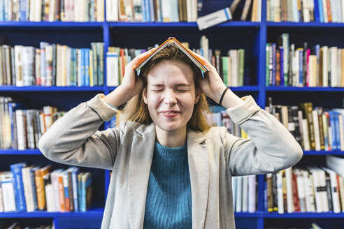 Porträt eines Teenagers mit einem Buch auf dem Kopf in einer öffentlichen Bibliothek - WPEF00501