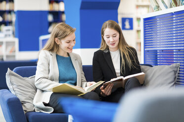 Two teenage girls sitting on couch in a public library reading books - WPEF00505